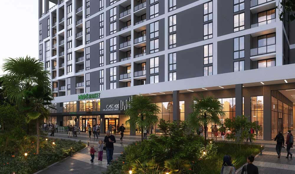 A modern multi-story apartment building with large windows and balconies. The ground floor features shops, including a VIBA MART and CASCADE. People are walking on a landscaped pathway with greenery and lights in front.