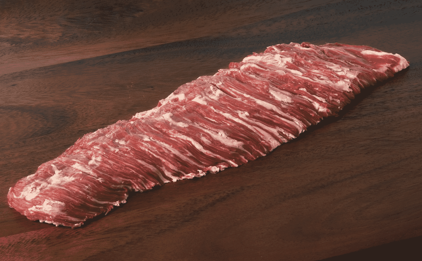 A raw skirt steak with visible marbling rests on a dark wooden surface, showcasing its long, flat shape and rich red color—a prime example often highlighted in any beef cuts guide.