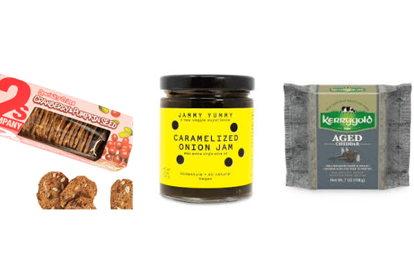 A package of cranberry pumpkin seed crisps, a jar of caramelized onion jam, and a block of Kerrygold aged cheddar cheese are displayed side by side on a white background—perfect for delightful cheese pairings or a memorable cheese tasting.