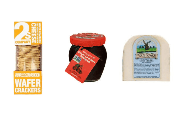 A box of sesame seed wafer crackers, a jar of sour cherry spread, and a wedge of goat cheese—perfect cheese pairings—are all displayed side by side on a white background.