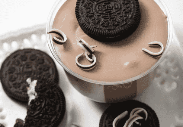 A cup of chocolate mousse topped with an Oreo cookie and white chocolate curls, served alongside locally baked Oreo cookies on a white plate—perfect for lovers of baked sweets.